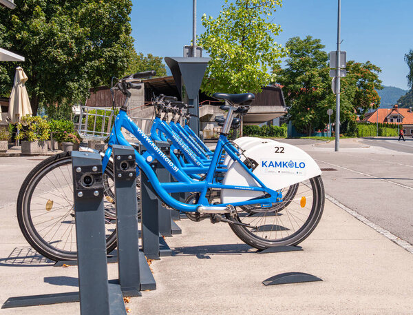 Камник, Словения - 10 августа 2025 года: Ряд голубых велосипедов, припаркованных на станции совместного пользования велосипедами в солнечный день.