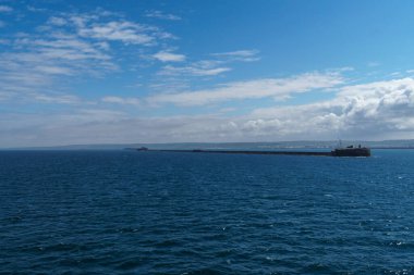 Gökyüzünde kabarık beyaz bulutlar olan huzurlu, mavi bir okyanus üzerinde nefes kesici bir manzara. Cherbourg Limanı, Fransa.