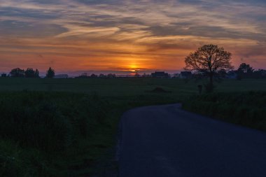 Huzurlu bir günbatımı, ufukta bulutların dolaştığı tarlalardan ve ağaçlardan oluşan sakin bir manzara çizer. Normandiya, Fransa. Mont St Michel yakınlarında..