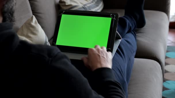 Een Man Die Thuis Bank Zit Een Groene Tablet Vasthoudt — Stockvideo