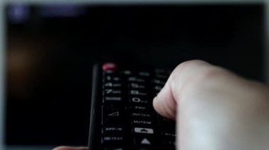 Kanal değiştirirken bir adamın tuttuğu uzaktan kumandanın yakın plan görüntüsü.