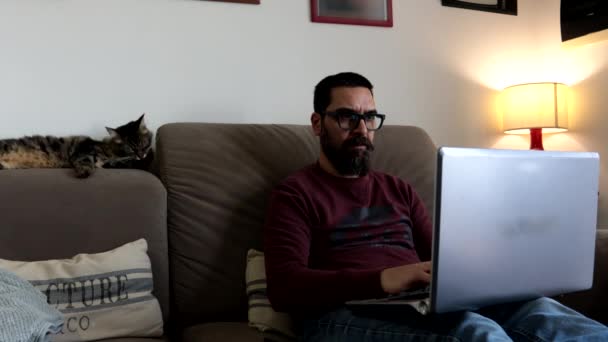 自宅のソファーに座っている男は キーボードにタイプするノートパソコンで動作します — ストック動画