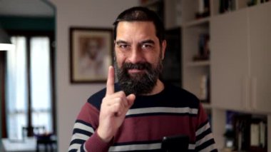 Sakallı adam güvenle kamerayı işaret ederek gülümsüyor..