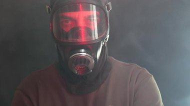 Geceleri duman ve sis içinde gaz maskesi takan adam kameraya bakıyor..