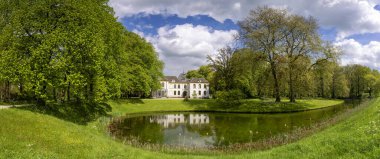 View at manor house te Baak reflecting in its moat and surrounded by beautiful trees with fresh green leaves clipart