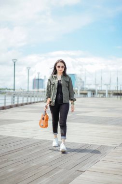 Ceket ve açık havada siyah kot giyen güzel bir Asyalı kadının Ukulele 'sini oynuyorum.