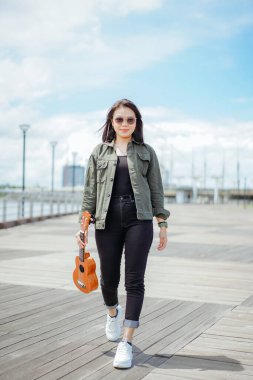 Ceket ve açık havada siyah kot giyen güzel bir Asyalı kadının Ukulele 'sini oynuyorum.