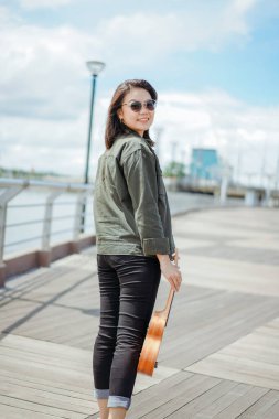 Ceket ve açık havada siyah kot giyen güzel bir Asyalı kadının Ukulele 'sini oynuyorum.