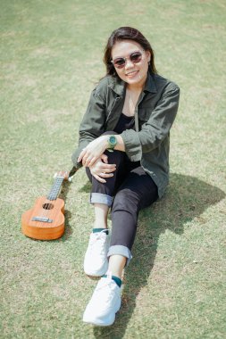 Ceket ve açık havada siyah kot giyen güzel bir Asyalı kadının Ukulele 'sini oynuyorum.