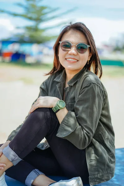 stock image Young Beautiful Asian Woman Wearing Jacket And Black Jeans Posing Outdoors Sitting on the park