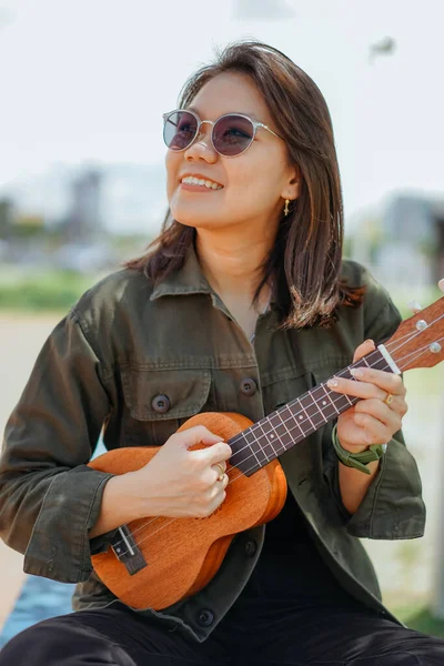 Играя Ukulele Молодой Красивой Азиатской Женщины Носить Куртку Черные Джинсы — стоковое фото