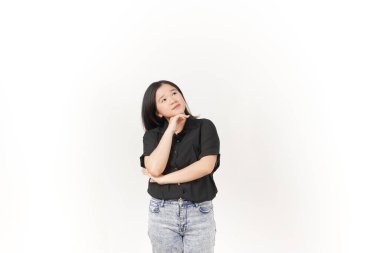 Genç Asyalı kadın beyaz arka planda siyah tişört ve kot pantolon giymeyi düşünüyor.