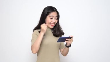 Güzel Asyalı Kadın, beyaz arka planda tek başına dikilirken akıllı telefondan mobil oyun oynuyor.