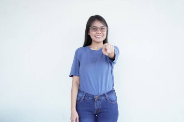 Güzel bir Asyalı kadın sana doğru bakarken sıcak bir şekilde gülümser. Beyaz bir arka plana karşı seni davet eden bir jest yapar.