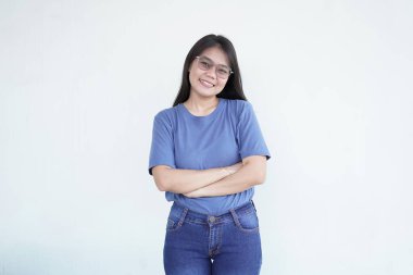 Güzel bir Asyalı kadın kollarını göğsünün üzerinde kavuşturarak beyaz bir arka plana karşı güvenini iletiyor.