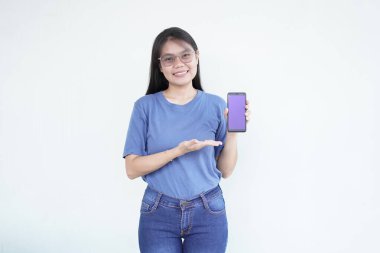 beautiful Asian woman smiles warmly while pointing to her smartphone, drawing attention to its screen against a white background clipart