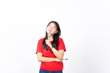 Güzel bir Asyalı kadın düşünceli bir poz verir, bir kaşık tutar ve onu beyaz arka planda çenesine yaslar.