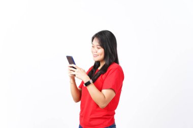 Beyaz arka planda izole edilmiş kırmızı tişört giyen güzel Asyalı kadının akıllı telefonunu kullanırken gülümse.