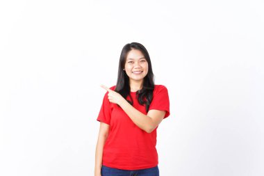 Gülümseyen, sunan ve işaret eden, beyaz arka planda izole edilmiş kırmızı tişörtlü, güzel Asyalı kadının reklamını yaptığı için.