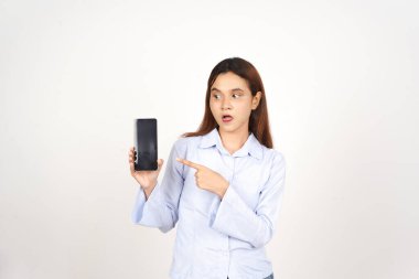 Beyaz arka planda izole edilmiş Asyalı güzel bir kadının akıllı telefonuna şaşırmış ve işaret ediyor.
