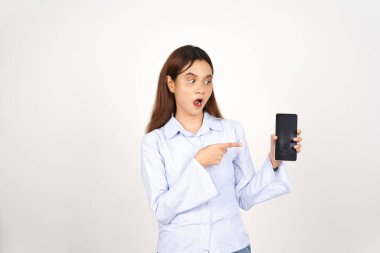 Beyaz arka planda izole edilmiş Asyalı güzel bir kadının akıllı telefonuna şaşırmış ve işaret ediyor.