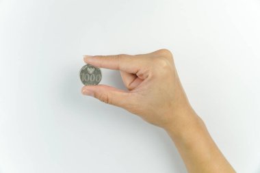 Beyaz arka planda 1000 Rupiah madeni para tutuyor.