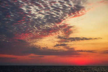 Gün batımında ya da denizde şafak vakti kırmızı lekeli güzel bulutlar. Okyanusun üzerinde dramatik gün doğumu gökyüzü.