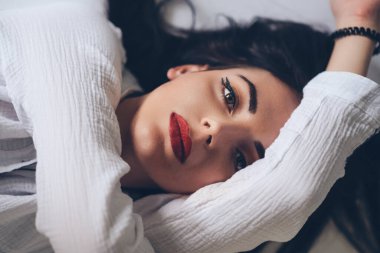 Kendini elleriyle kucaklayan esmer bir kız kameraya üzgün ve özlemle bakıyor..