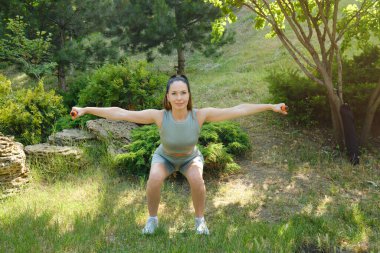 Kız parkta dambıllarla çömeliyor..