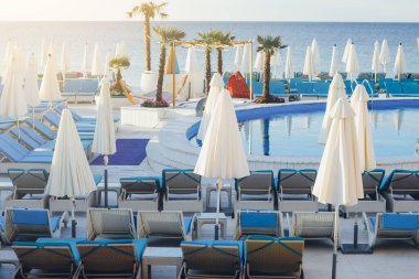 Yüzme havuzu, şemsiyeleri ve deniz zemininde güneşlenen boş tatil beldesi..