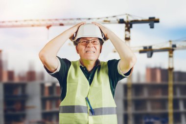 İnşaat alanı kazası. Foreman, yüzünde duygularla bir inşaat alanının arka planına tutunarak kafasını sıkıca tutuyor.