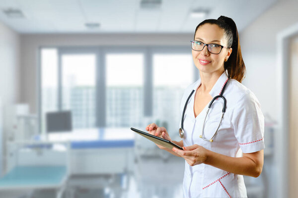 Girl doctor in glasses with a tablet on the background of a hospital ward. copy space.