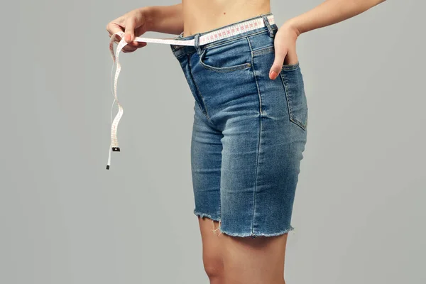 減量コンセプト 少女はデニムショートパンツのベルトの代わりにウエストの周りに包まれた測定テープを持っています クローズアップ — ストック写真