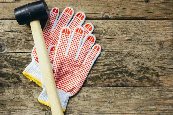 Rubber mallet and protective construction gloves on a wooden background with space for text.