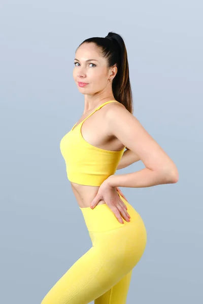 Fitness model in yellow sportswear on a gray background. Studio shot.