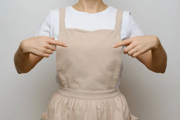 A girl in a beige apron points to her chest. Blank for design, place for text. Mockup.