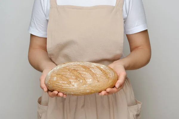 Dziewczyna Beżowym Fartuchu Trzyma Rękach Bochenek Domowego Chleba Zbliżenie Miejsce — Zdjęcie stockowe