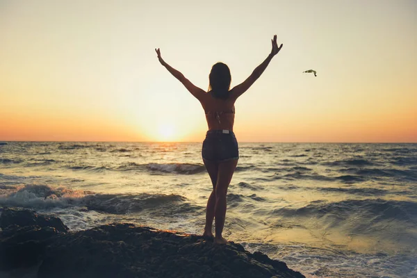Silhouette of a girl with outstretched arms against the backdrop of dawn over the sea or ocean.