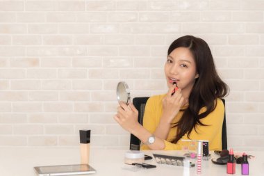 Gülümseyen Asyalı kadın makyaj masasında güzellik ürünleriyle otururken yüzünü kızartıyor..