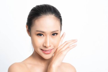 Asyalı bir kadın hassas bir el hareketiyle pürüzsüz cildini ön plana çıkarıyor. Etkili cilt bakımı özünü temsil ediyor. Ve beyaz arka planda doğal ışık saçan gençlik görüntüsü stüdyosu..