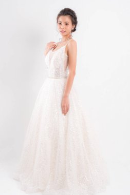 Beyaz gelinlik ve kolyeli güzel Asyalı gelin beyaz arka planda stüdyo çekimlerinde zarif bir poz veriyor..