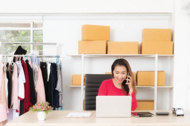 Neşeli bir girişimci telefona cevap verirken gülümser ve bilgisayarında çalışır. Başarılı online mağazası için müşteri siparişlerini işler..