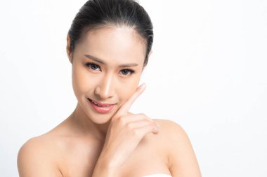 Asyalı bir kadın hassas bir el hareketiyle pürüzsüz cildini ön plana çıkarıyor. Etkili cilt bakımı özünü temsil ediyor. Ve beyaz arka planda doğal ışık saçan gençlik görüntüsü stüdyosu..