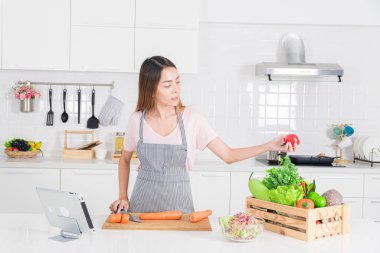 Şık bir mutfakta çekici bir kadın sağlıklı ve dengeli bir yaşam tarzını vurgulayan havuç, marul ve elma gibi taze sebzeleri hazırlamaya odaklanır..