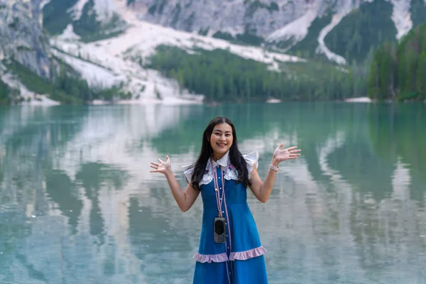 portrait of happy Asian woman tourist with background of Braies lake with mountains. Dolomites, Italy.  famous lake with beautiful reflection in water, trees. Travel.