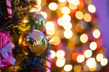 Geleneksel süslemelerle süslenmiş bir Noel ağacının yakınında gümüş yaylı kırmızı hediyeler, şeker kamışları, altın mücevherler ve şenlikli bir parıltı yaratan ışıklar..