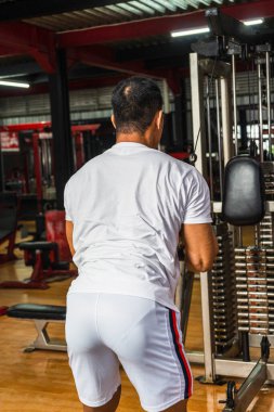 Spor salonunda ağırlık kaldıran, beyaz gömlekli bir sporcunun arkası.