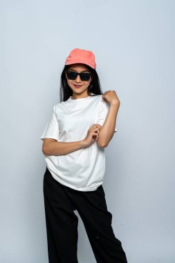 Beyaz gömlekli ve gözlüklü genç bir kadın beyaz arka planda gülümserken havalı bir poz veriyor.