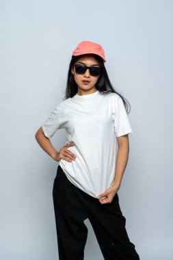 Beyaz gömlekli ve gözlüklü genç bir kadın beyaz arka planda havalı bir poz veriyor.