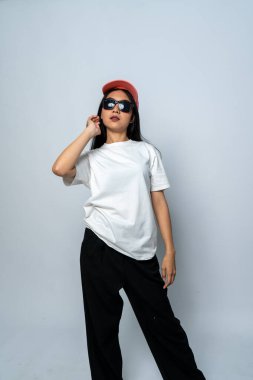 Beyaz gömlekli ve gözlüklü genç bir kadın beyaz arka planda havalı bir poz veriyor.